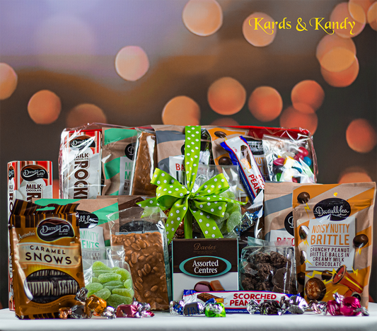 The Golden Delight Hamper by Zen Eunoia offers a festive assortment of chocolates and candies in vibrant packaging, making it an ideal choice for corporate gifts. The arrangement is elegantly adorned with a green ribbon, set against a blurred, warm-toned bokeh background, with the words "Kards & Kandy" featured in the top right corner.